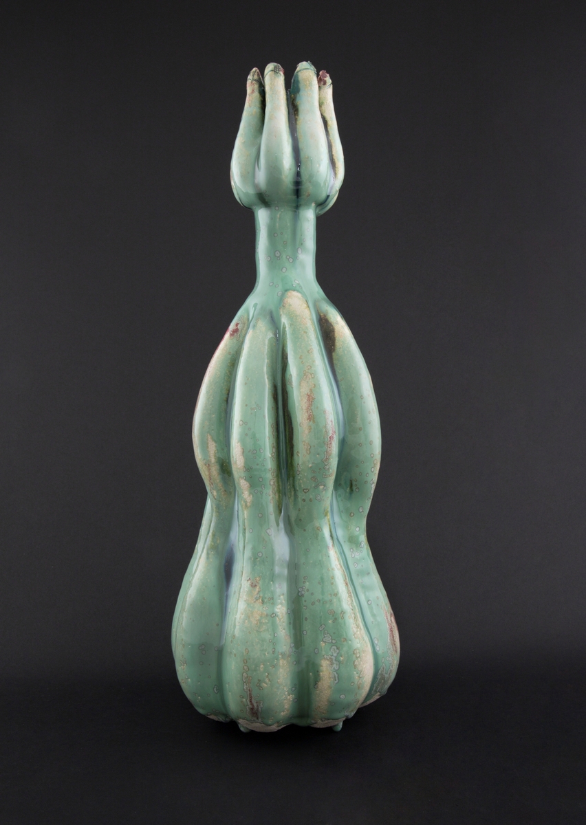 Håndmodellert skulptur i glasert steingods med oppreist holdning. Den har en organisk og asymmetrisk kalebassform som ender i en tulipanform med halvåpne kronblader. Keramikkskulpturen inngår i en installasjon bestående av 26 deler i ulike størrelser og med individuell utforming. De asymmetriske variasjonene gir et inntrykk av bevegelse, og den lett sykelige fargepaletten gir et uhyggelig og grotesk preg. Samtlige deler minner om kjøttetende planter.