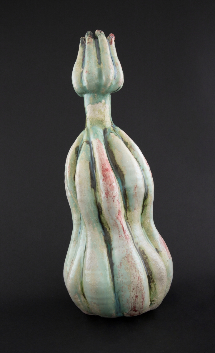 Håndmodellert skulptur i glasert steingods med oppreist holdning. Den har en organisk og asymmetrisk kalebassform som ender i en tulipanform med halvåpne kronblader. Keramikkskulpturen inngår i en installasjon bestående av 26 deler i ulike størrelser og med individuell utforming. De asymmetriske variasjonene gir et inntrykk av bevegelse, og den lett sykelige fargepaletten gir et uhyggelig og grotesk preg. Samtlige deler minner om kjøttetende planter.