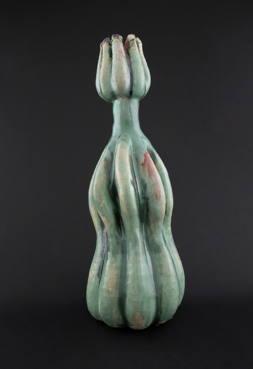 Håndmodellert skulptur i glasert steingods med oppreist holdning. Den har en organisk og asymmetrisk kalebassform som ender i en tulipanform med halvåpne kronblader. Keramikkskulpturen inngår i en installasjon bestående av 26 deler i ulike størrelser og med individuell utforming. De asymmetriske variasjonene gir et inntrykk av bevegelse, og den lett sykelige fargepaletten gir et uhyggelig og grotesk preg. Samtlige deler minner om kjøttetende planter.