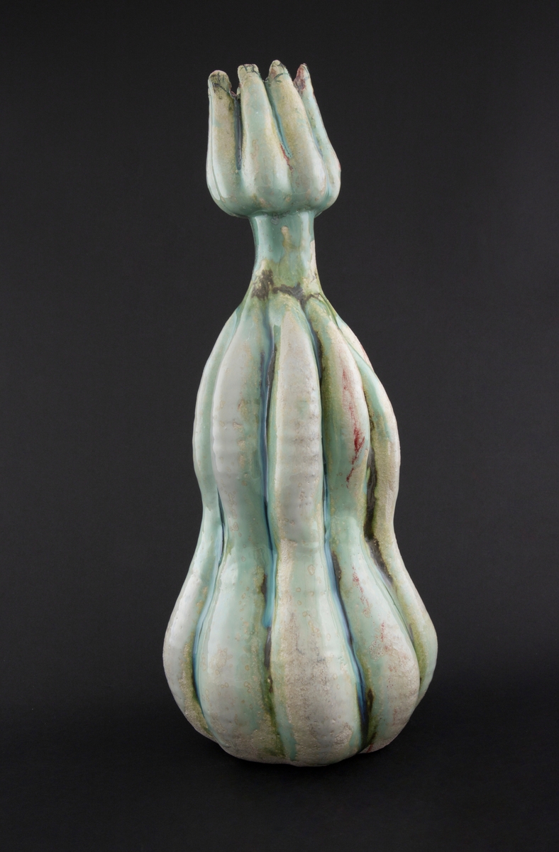 Håndmodellert skulptur i glasert steingods med oppreist holdning. Den har en organisk og asymmetrisk kalebassform som ender i en tulipanform med halvåpne kronblader. Keramikkskulpturen inngår i en installasjon bestående av 26 deler i ulike størrelser og med individuell utforming. De asymmetriske variasjonene gir et inntrykk av bevegelse, og den lett sykelige fargepaletten gir et uhyggelig og grotesk preg. Samtlige deler minner om kjøttetende planter.