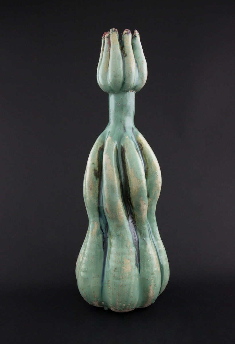 Håndmodellert skulptur i glasert steingods med oppreist holdning. Den har en organisk og asymmetrisk kalebassform som ender i en tulipanform med halvåpne kronblader. Keramikkskulpturen inngår i en installasjon bestående av 26 deler i ulike størrelser og med individuell utforming. De asymmetriske variasjonene gir et inntrykk av bevegelse, og den lett sykelige fargepaletten gir et uhyggelig og grotesk preg. Samtlige deler minner om kjøttetende planter.