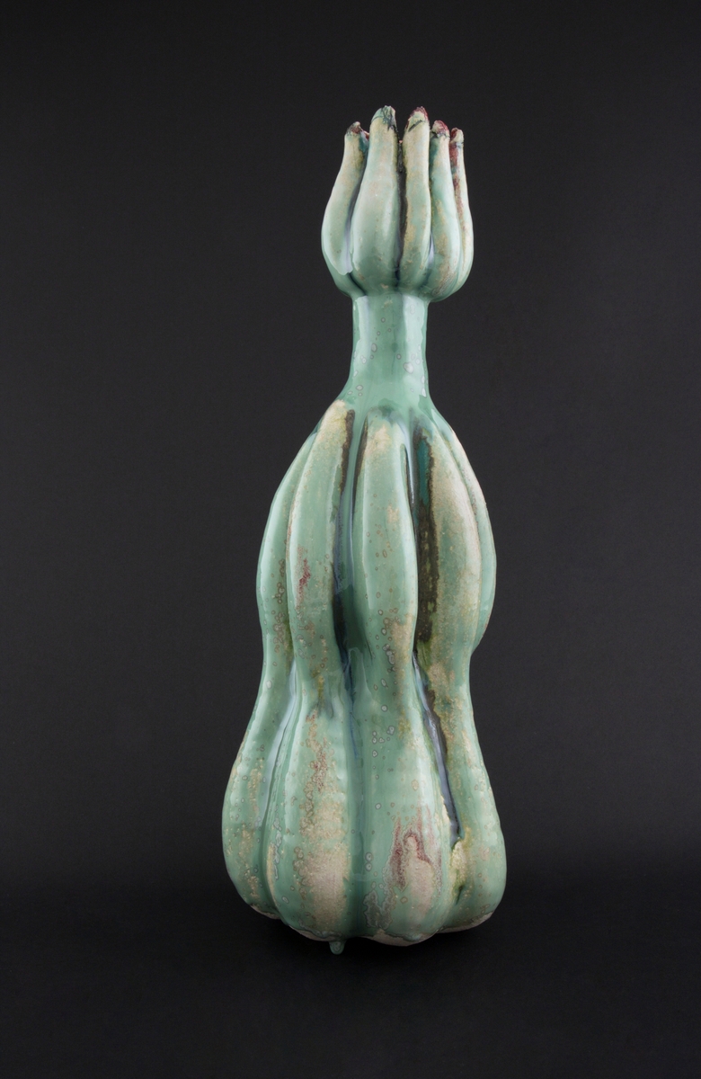 Håndmodellert skulptur i glasert steingods med oppreist holdning. Den har en organisk og asymmetrisk kalebassform som ender i en tulipanform med halvåpne kronblader. Keramikkskulpturen inngår i en installasjon bestående av 26 deler i ulike størrelser og med individuell utforming. De asymmetriske variasjonene gir et inntrykk av bevegelse, og den lett sykelige fargepaletten gir et uhyggelig og grotesk preg. Samtlige deler minner om kjøttetende planter.