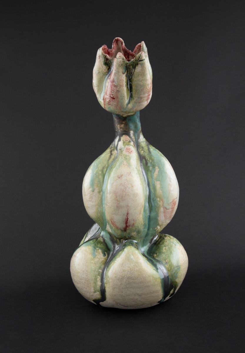 Håndmodellert skulptur i glasert steingods med oppreist holdning. Den har en organisk og asymmetrisk kalebassform som ender i en tulipanform med halvåpne kronblader. Keramikkskulpturen inngår i en installasjon bestående av 26 deler i ulike størrelser og med individuell utforming. De asymmetriske variasjonene gir et inntrykk av bevegelse, og den lett sykelige fargepaletten gir et uhyggelig og grotesk preg. Samtlige deler minner om kjøttetende planter.