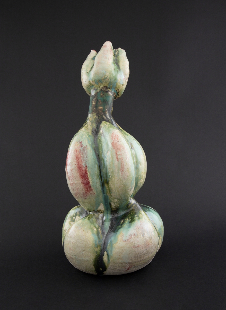 Håndmodellert skulptur i glasert steingods med oppreist holdning. Den har en organisk og asymmetrisk kalebassform som ender i en tulipanform med halvåpne kronblader. Keramikkskulpturen inngår i en installasjon bestående av 26 deler i ulike størrelser og med individuell utforming. De asymmetriske variasjonene gir et inntrykk av bevegelse, og den lett sykelige fargepaletten gir et uhyggelig og grotesk preg. Samtlige deler minner om kjøttetende planter.