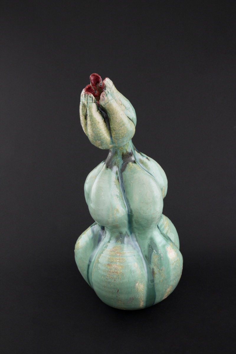 Håndmodellert skulptur i glasert steingods med oppreist holdning. Den har en organisk og asymmetrisk kalebassform som ender i en tulipanform med halvåpne kronblader. Keramikkskulpturen inngår i en installasjon bestående av 26 deler i ulike størrelser og med individuell utforming. De asymmetriske variasjonene gir et inntrykk av bevegelse, og den lett sykelige fargepaletten gir et uhyggelig og grotesk preg. Samtlige deler minner om kjøttetende planter.