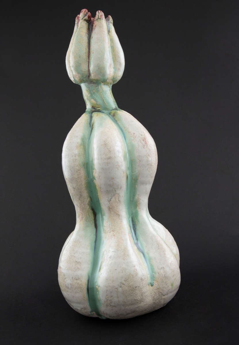 Håndmodellert skulptur i glasert steingods med oppreist holdning. Den har en organisk og asymmetrisk kalebassform som ender i en tulipanform med halvåpne kronblader. Keramikkskulpturen inngår i en installasjon bestående av 26 deler i ulike størrelser og med individuell utforming. De asymmetriske variasjonene gir et inntrykk av bevegelse, og den lett sykelige fargepaletten gir et uhyggelig og grotesk preg. Samtlige deler minner om kjøttetende planter.