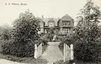 S.A. Nilsson, Braås. En större villa med trädgård, ca 1900. En man och en kvinna står framför huset med en liten flicka.