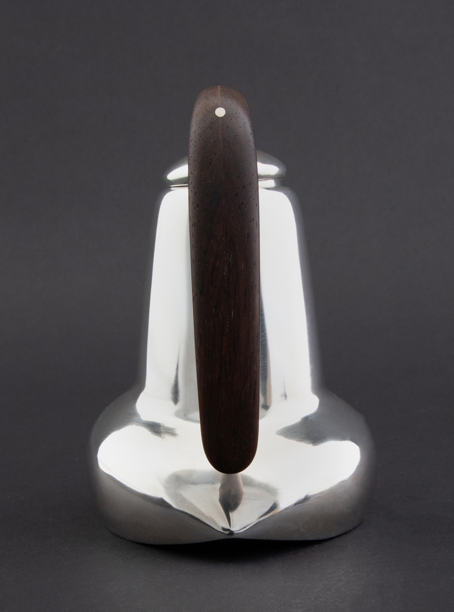 Kanne i sølv med håndtak av palisander. Ovalformet korpus samt høyreist hals med fremtrukket tut. Mykt buet håndtak samt lokknapp i palisander. Samtlige deler preges av mykt avrundede kanter. Innsiden er forgylt.