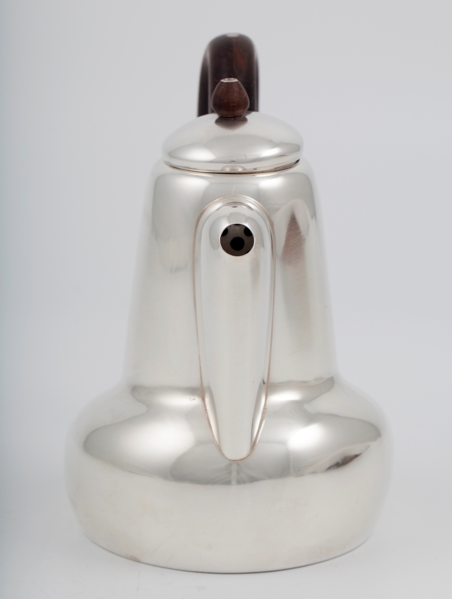 Kanne i sølv med håndtak av palisander. Ovalformet korpus samt høyreist hals med fremtrukket tut. Mykt buet håndtak samt lokknapp i palisander. Samtlige deler preges av mykt avrundede kanter. Innsiden er forgylt.