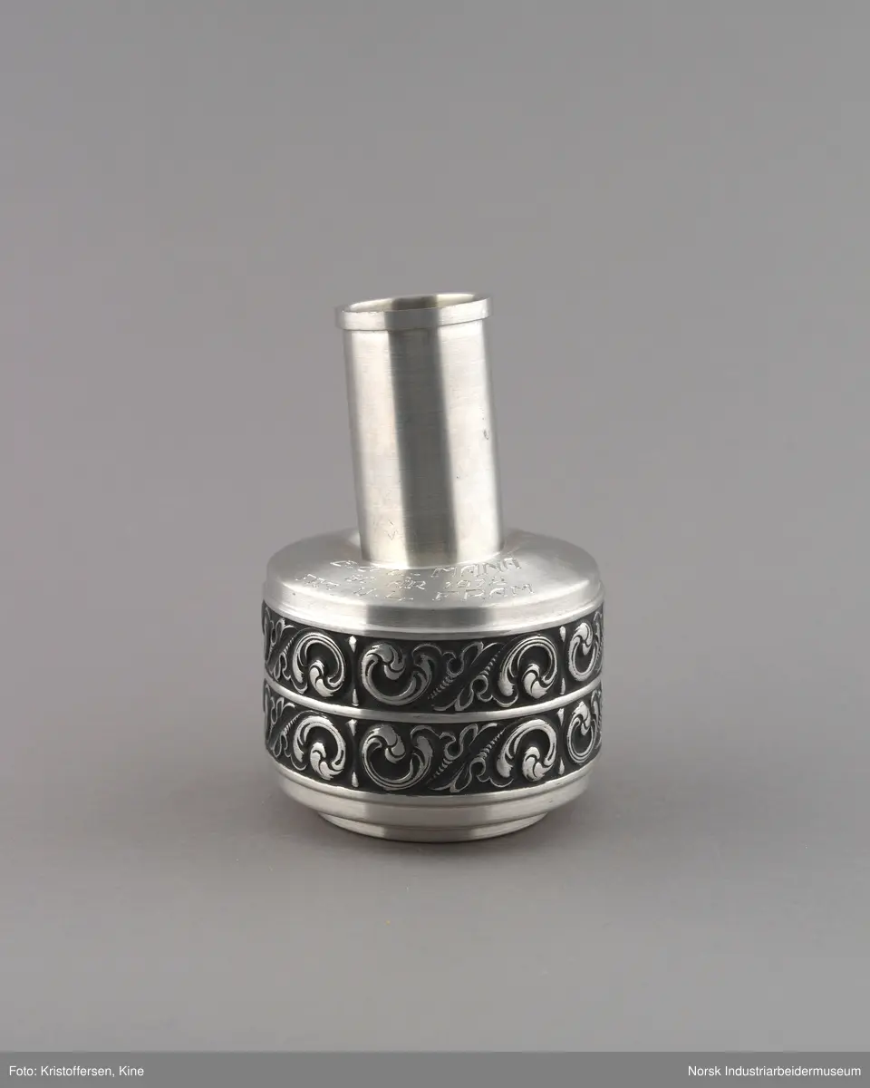 Vase eller pokal ned gravert innskrift til Bondeungdomslaget Maana i norsk tinn. Vasen er sirkulær med repeterende ornamentikk på to langsgående bånd rundt vasen. Hals er smal og sirkulær