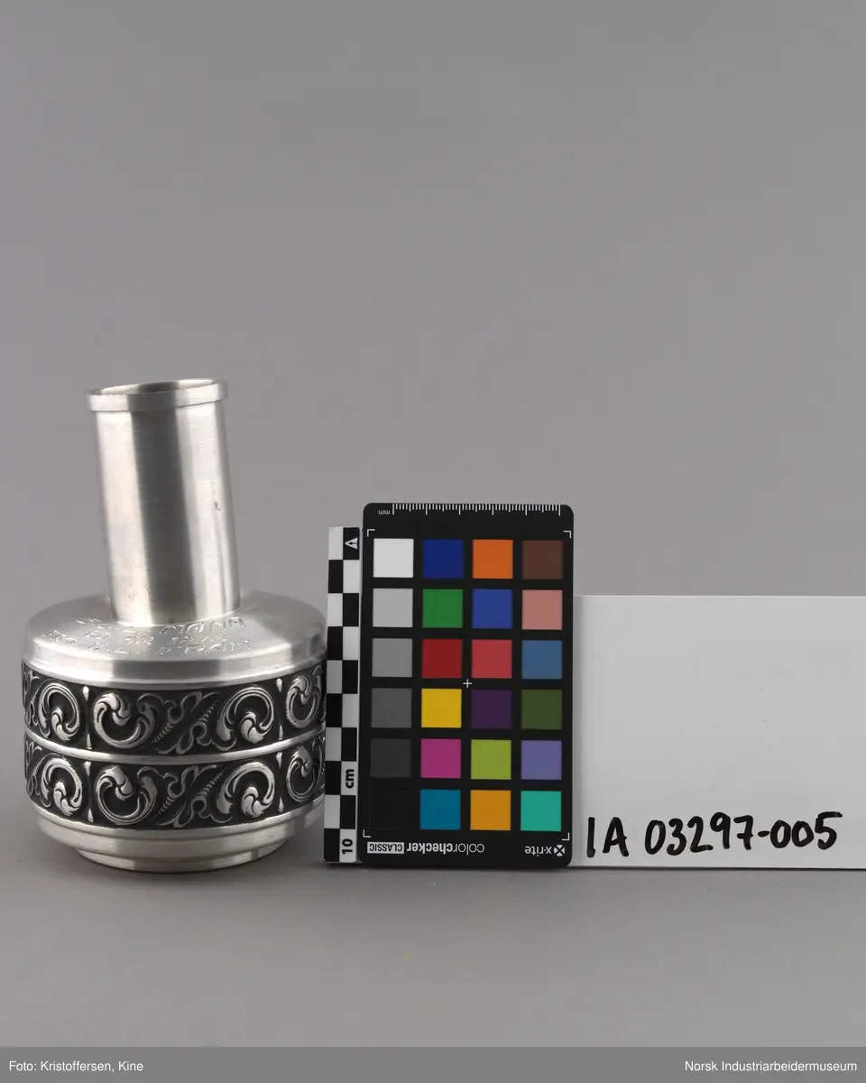 Vase eller pokal ned gravert innskrift til Bondeungdomslaget Maana i norsk tinn. Vasen er sirkulær med repeterende ornamentikk på to langsgående bånd rundt vasen. Hals er smal og sirkulær