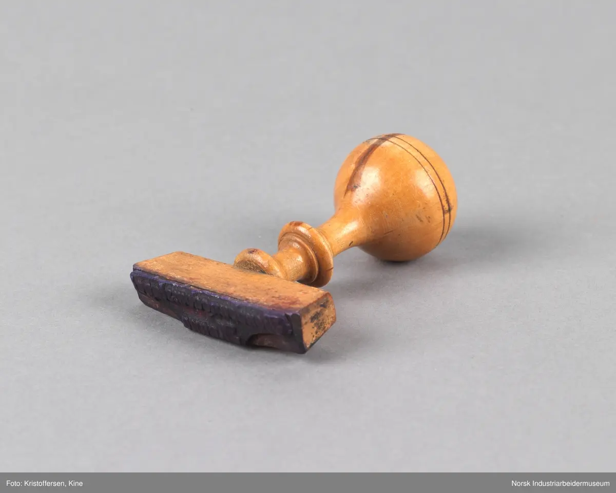 Stempel i tre med rundt håndtak og tverrgående stempelhode. Stempelpute med utheving av skriften "Bondeungdomslaget Maana".