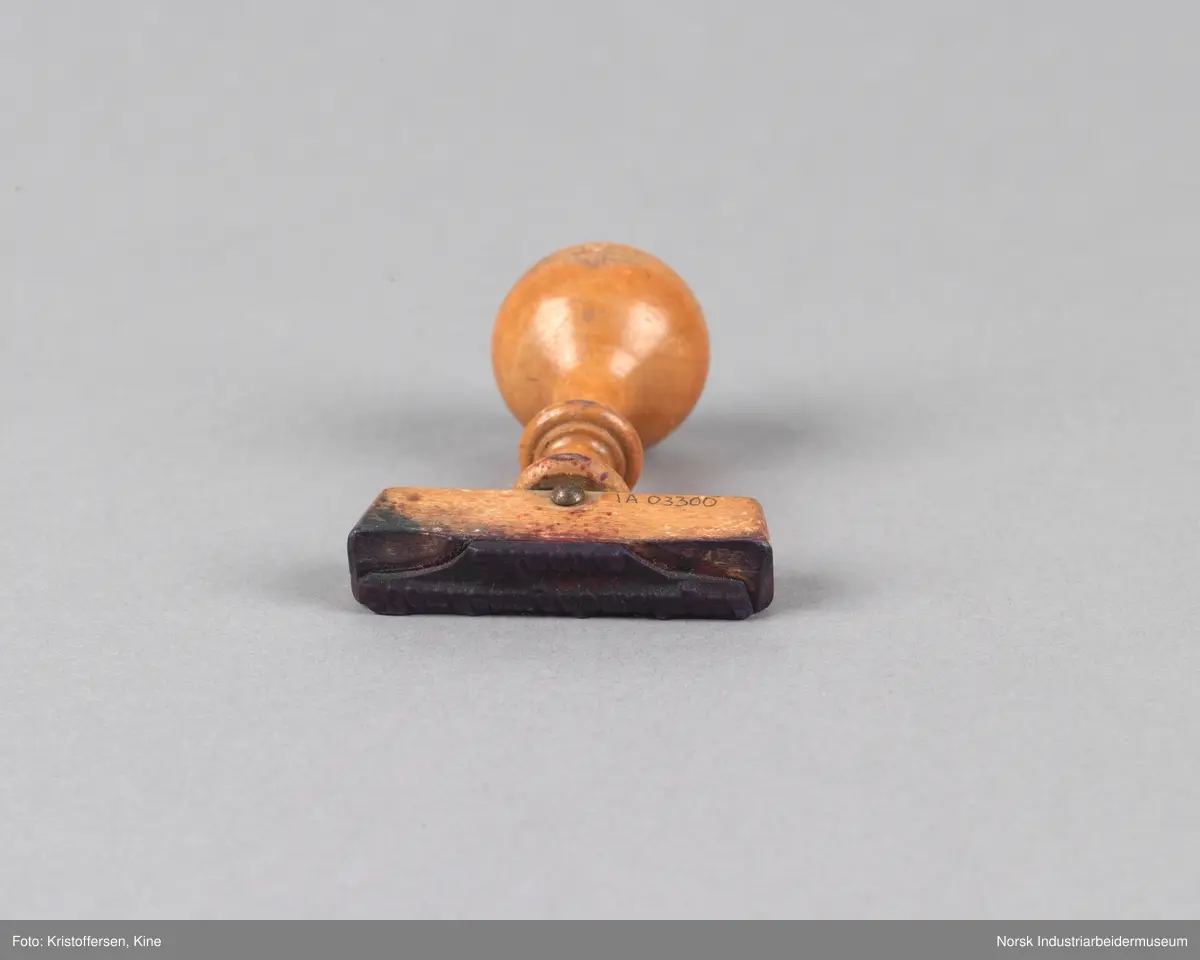 Stempel i tre med rundt håndtak og tverrgående stempelhode. Stempelpute med utheving av skriften "Bondeungdomslaget Maana".