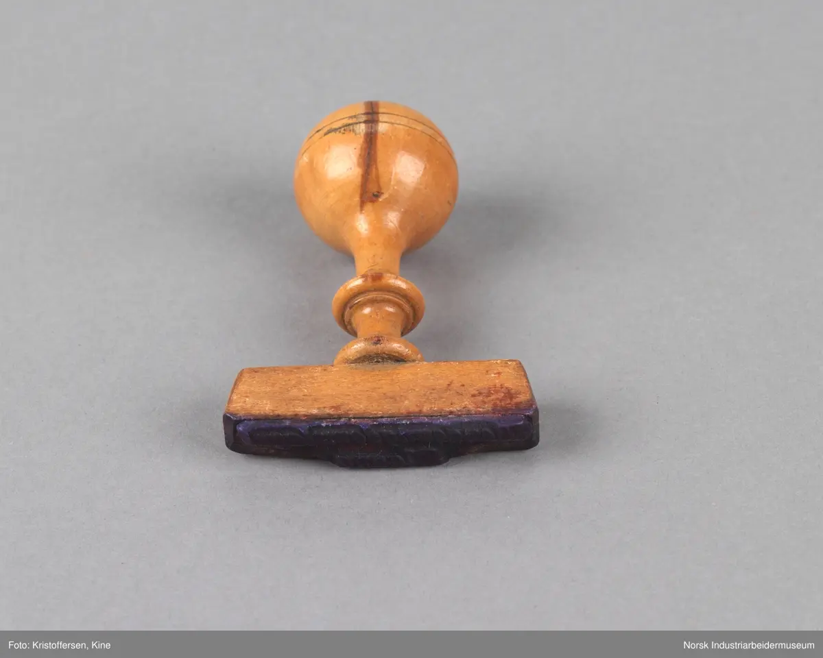 Stempel i tre med rundt håndtak og tverrgående stempelhode. Stempelpute med utheving av skriften "Bondeungdomslaget Maana".