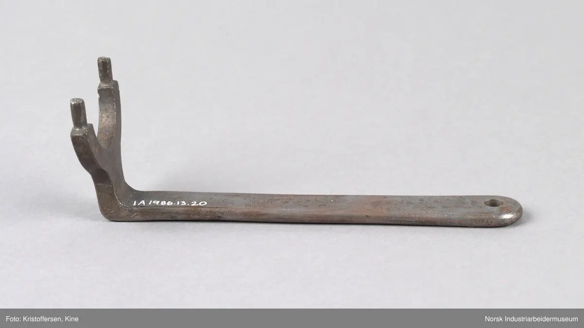Akselmutternøkkel med 39 mm åpning. Avrundt skaft med hull i enden. Hode er bøyd og har en u-formet bøy i åpningen og to mintre tagger som stikker opp på hver side