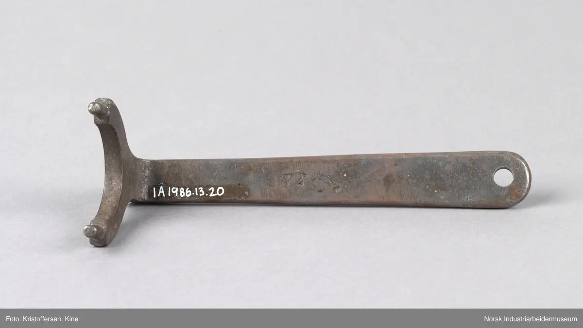 Akselmutternøkkel med 39 mm åpning. Avrundt skaft med hull i enden. Hode er bøyd og har en u-formet bøy i åpningen og to mintre tagger som stikker opp på hver side
