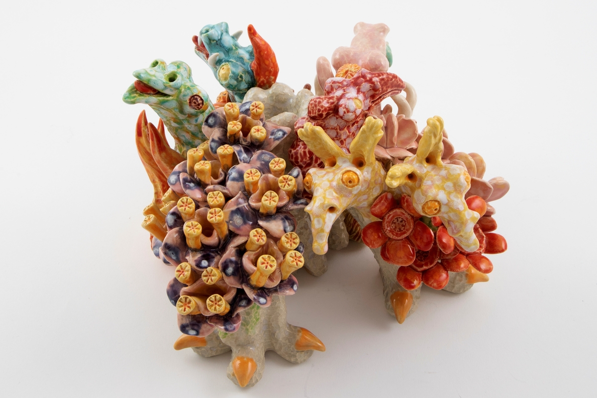 Komponert av fantasifigurer som minner om undervannsdyr, drager og flodhester.  Blomster og koraler. To dyreføtter med klør ut fra korpus.