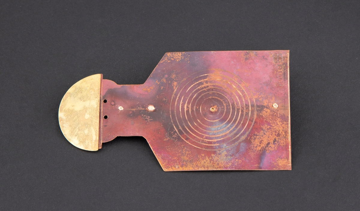 Brosje som forestiller en person med blink på brystet. Personen har gullhat og rødlig kobberkrop. Blink på brystet.