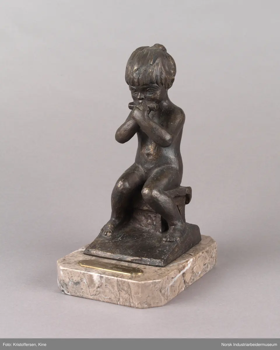 Tinn kommunes kulturpris, "Liten Ida" av kunstner Kjell Grette Christensen. Bronseskulptur av liten jente som sitter på en krakk og spiser noe med begge hendene. Skulpturen er festet på en firkantet steinplate uten hjørner. På steinplaten er det festet en plakett for Tinn kommunes kulturpris