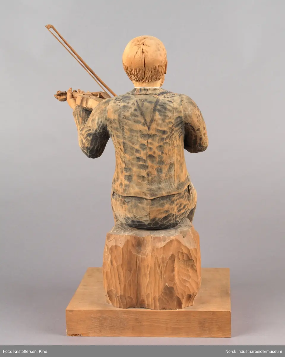 Utskjært treskulptur av spelemannen Knut Johannessen Dahle. Figuren sitter på en kasse med en hardingfele i venstre hånd og en løs bue i den høyre. Han har på seg finklær, sko og sløyfe. Hodet er utskjært med blant annet skjegg, bart og måne. Navnet til Dahle er inngravert på platen.