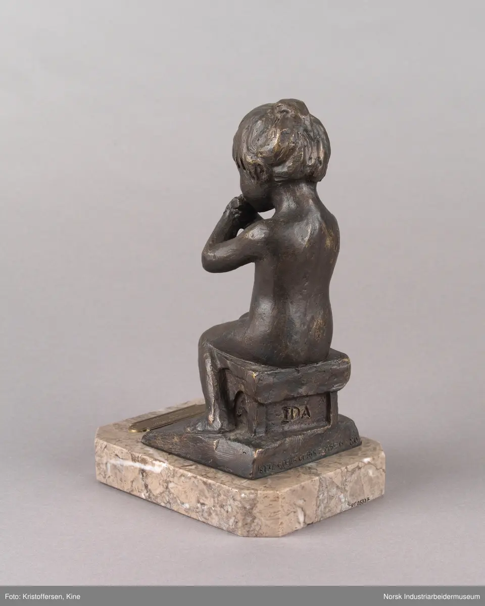 Tinn kommunes kulturpris, "Liten Ida" av kunstner Kjell Grette Christensen. Bronseskulptur av liten jente som sitter på en krakk og spiser noe med begge hendene. Skulpturen er festet på en firkantet steinplate uten hjørner. På steinplaten er det festet en plakett for Tinn kommunes kulturpris