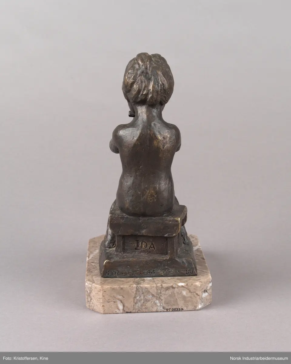 Tinn kommunes kulturpris, "Liten Ida" av kunstner Kjell Grette Christensen. Bronseskulptur av liten jente som sitter på en krakk og spiser noe med begge hendene. Skulpturen er festet på en firkantet steinplate uten hjørner. På steinplaten er det festet en plakett for Tinn kommunes kulturpris