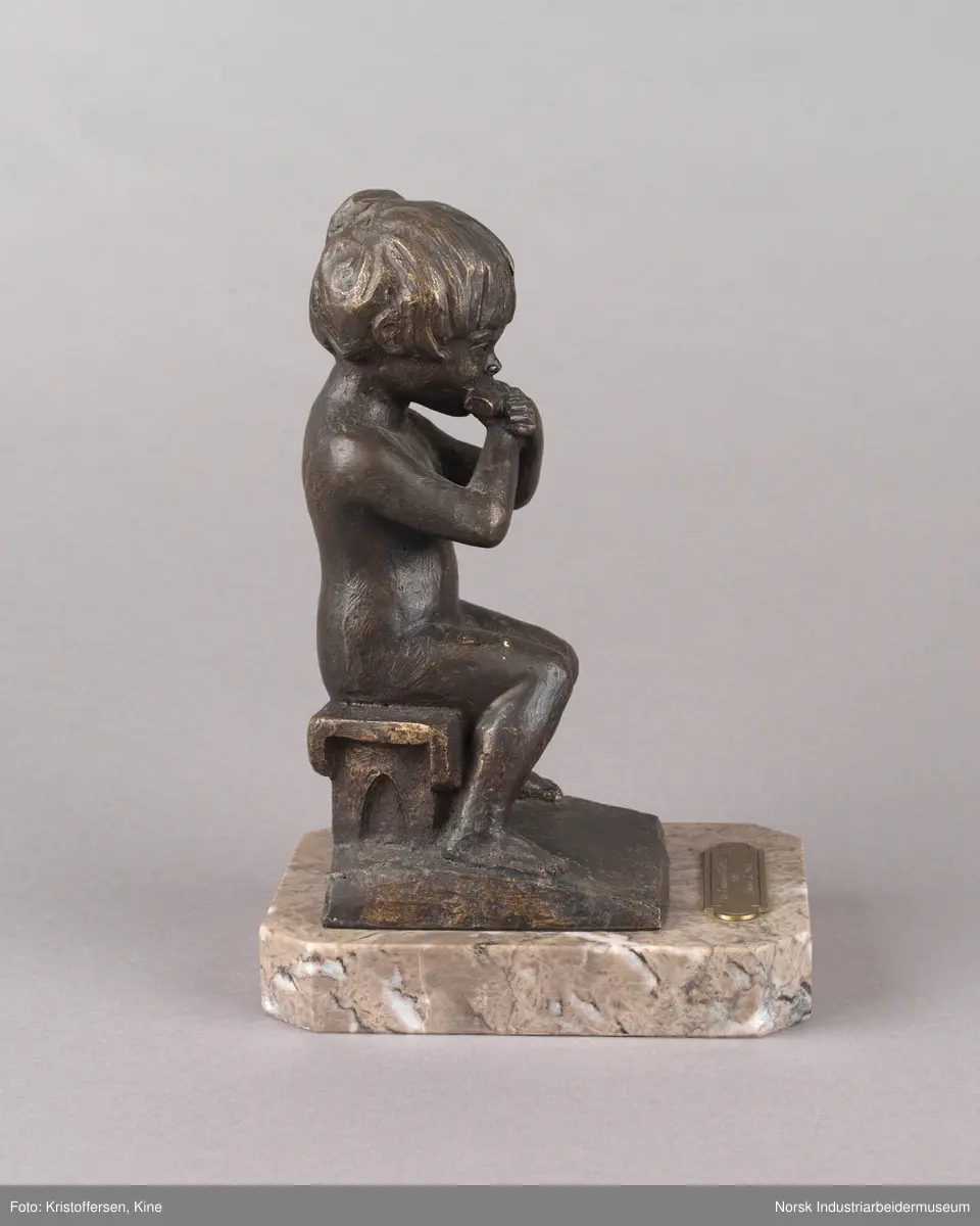Tinn kommunes kulturpris, "Liten Ida" av kunstner Kjell Grette Christensen. Bronseskulptur av liten jente som sitter på en krakk og spiser noe med begge hendene. Skulpturen er festet på en firkantet steinplate uten hjørner. På steinplaten er det festet en plakett for Tinn kommunes kulturpris