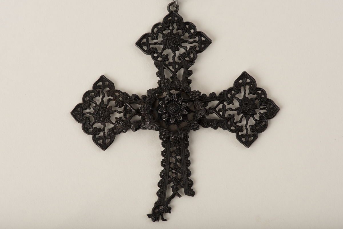 Svart halsband av gjutjärn.
Halsbandet består av omväxlande större och mindre utsirade länkar i nygotisk stil, som är sammanfästa med runda små länkar. Mitt fram hänger ett större likformat kors, som är något skadat. Spännet är utformat som två händer.