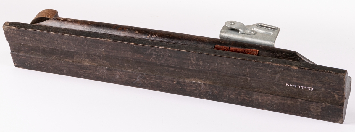 Skidbindningsprov. Vit metallegering på underlag av mörkbrunfärgat trä. På ovasidan Elof Malmbergs firmamärke i metall. Rund metallkantad etikett med skriften "2001 M   N. 7/75" Märke på metalldelen "HOBBY".