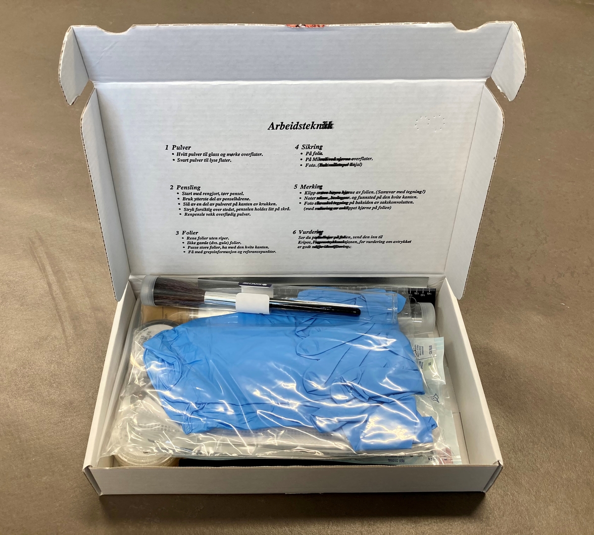 Pappeske med sterilt utstyr for sikring av fingeravtrykk fra åsteder. Settett innholder hvitt og sort fingeravtrykkspulver, pensler, målestokk, steriliseringsservietter, saks, penn, åndedrettsmaske (munnbind) fingeravtrykksfolie, skjema, engangshansker.