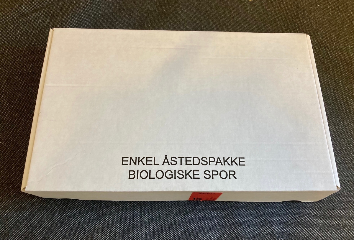 Åstedspakke i papp. Imnneholder skjema og sterilt utstyr for sikring av biologiske spor; bevisposer, bomullspinner, sterilt laken, engangshansker, steriliseringsservietter, munnbind, engangspinsett, sterilt saltvann, forseglingstape.