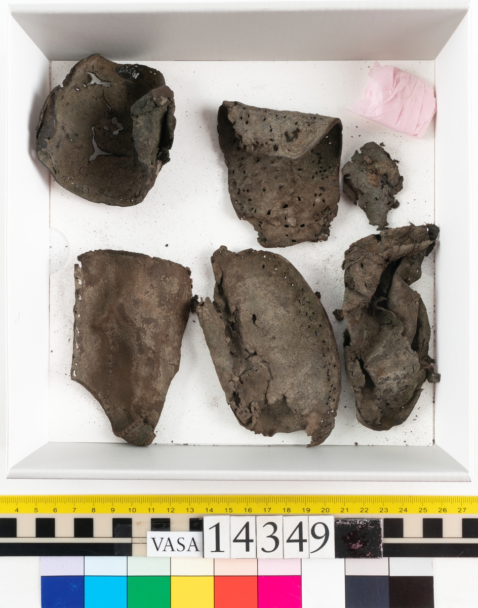 Sex delar från sko. Ett sidostycke med en kvarsittande bit av slejfen samt fem delar från skobotten i form av sulor mm. Lädret är spaltat och mycket sprött.