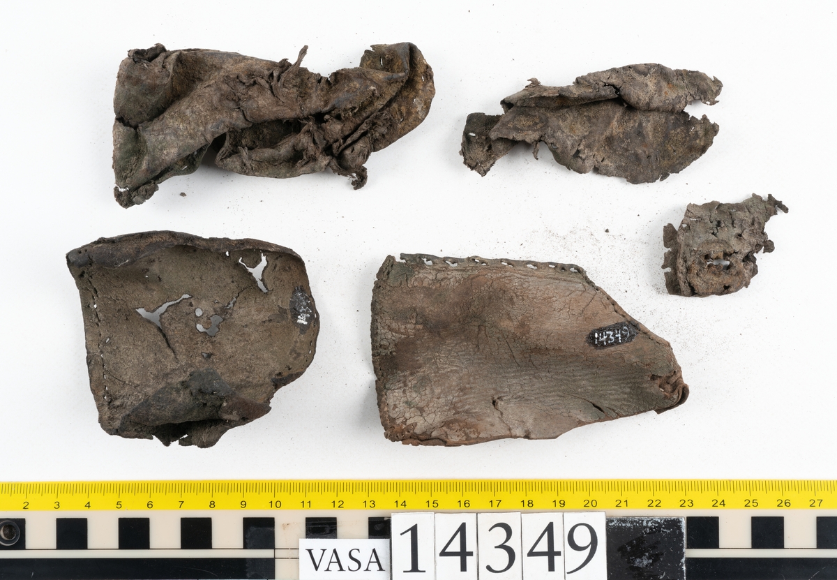 Sex delar från sko. Ett sidostycke med en kvarsittande bit av slejfen samt fem delar från skobotten i form av sulor mm. Lädret är spaltat och mycket sprött.