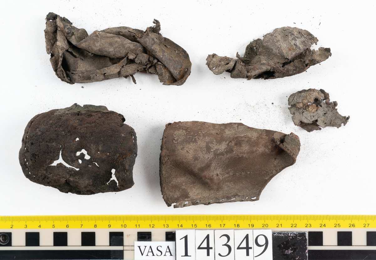 Sex delar från sko. Ett sidostycke med en kvarsittande bit av slejfen samt fem delar från skobotten i form av sulor mm. Lädret är spaltat och mycket sprött.