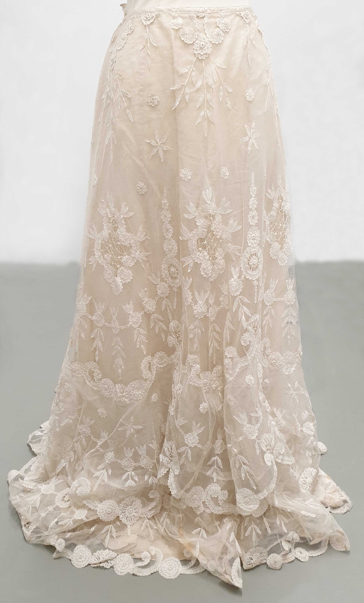 Kjolen av to deler - skjørt med påkneppet bluse.
Blusen er i organza og tyll med formede rosetter av blonder i metervis, påsydd en og en. Et bredt gullbånd med knute i enden rundt halsutringing. Blusen har korte puffermer, med blonder. Skjørtet har slep og består av tyll med broderte rosetter.