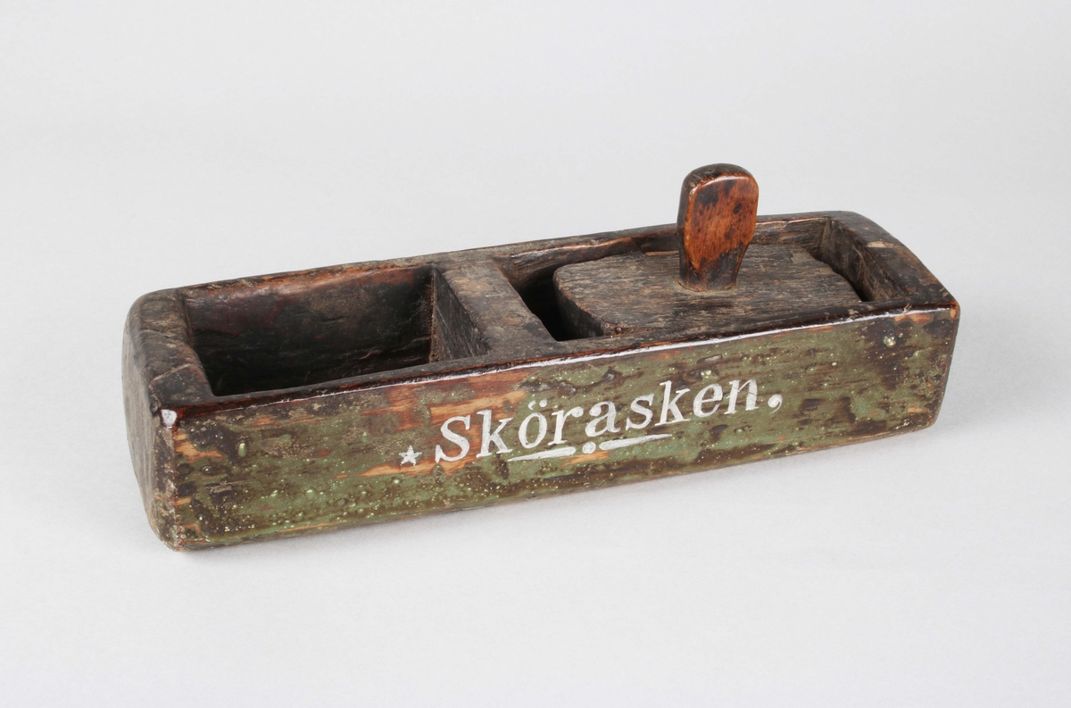 Skörask. Grönmålad, avlång, rektangulär låda med delning, där det mindre utrymmet användes för förvaring av elddon. Skuret rektangulärt lock med avlång knopp, för det utrymmet som är ämnat för luftcirkulation. Fnöske som antändnings-material. Eldstål av smitt järn medföljer.
Bruks- färg och åldersslitage.

Funktion: Eldstål för att göra upp eld, samt ask för förvaring av fnöske
