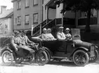 En bil (cabriolet) av märket Cadillac och en motorcykel av märket Indian med sidovagn står på Brahegatan i Gränna, riktning söderut. I bilen sitter en man (bakom ratten) och tre kvinnor på motorcykeln sitter två män.
De står på gatan nedanför före detta Amalia Eriksons polkagriskokeri.