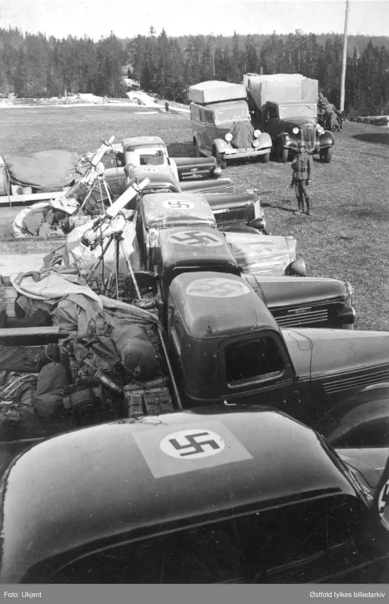 Tyske tropper i Gudbrandsdalen i april 1940. Oppstilt rad av  rekvirerte, norske lastebiler og personbil med hakekors på taket av førerhuset. Våpen på lasteplan er Colt mitraljøse m/29.
Nærmest og bakover: Uidentifisert amerikansk personbil 1937-39, fire lastebiler: Ford (?) 1938-39, Oldsmobile 1938, Chevrolet 1936, Fargo 1937-38, Opel Kaptein personbil 1939. To av lastebilene har våpen på lasteplanet. 
Bak, fra venstre: Ukjent varebil, Chevrolet lastebil 1937. Sivile norske biler, rekvirert av tyskerne og påmalt hakekors for å unngå angrep fra eget flyvåpen (Luftwaffe).