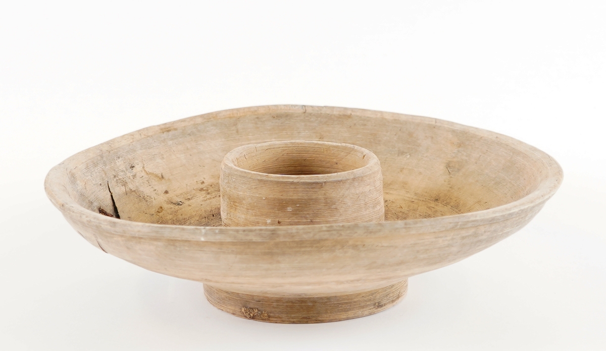 Eit dreia fat, med ei lita skål i midten av same trestykke. Stett under. To metallklamper er sett på som reperasjon av sprekk. Den vesle skåla i midten vart nytta til å ha feitt til maten oppi.