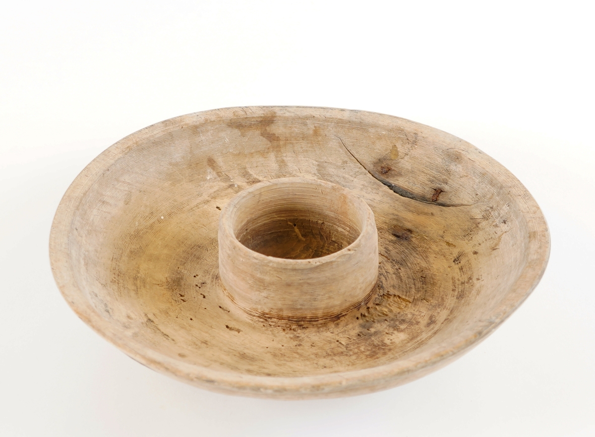 Eit dreia fat, med ei lita skål i midten av same trestykke. Stett under. To metallklamper er sett på som reperasjon av sprekk. Den vesle skåla i midten vart nytta til å ha feitt til maten oppi.