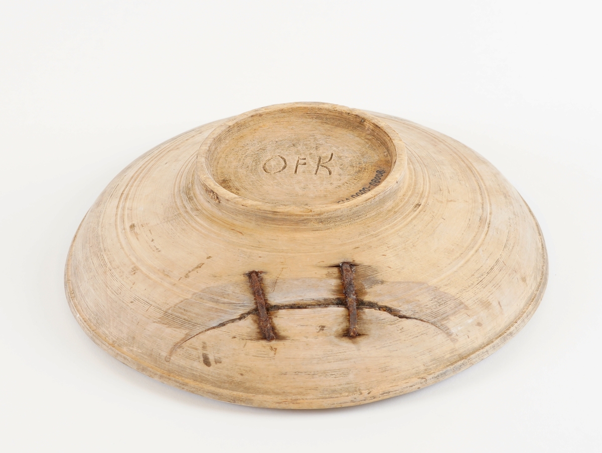 Eit dreia fat, med ei lita skål i midten av same trestykke. Stett under. To metallklamper er sett på som reperasjon av sprekk. Den vesle skåla i midten vart nytta til å ha feitt til maten oppi.