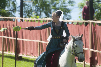 Kvinne på hest i blågrønn houppelandkjole med sverd som kapper et kålhode i to