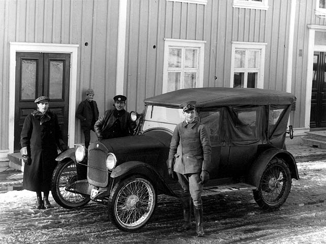 "Eklund med sin hyrbil". En bil står parkerad utanför Hotell Brahe i Gränna. Det är en Hupmobil med registreringsnr F327. Hitom bilen står en man i chaufförsuniform, möjligen Eklund. Till vänster vid bilens front står en man i keps och rock med pälskrage, det är chaufför Harry Håkansson. Bakom bilen står en okänd man i keps, skinnjacka och troligen uniform - Harry Siebke? Mot husväggen står en pojk med pälsmössa och ler mot fotografen, möjligen David Ebbesson. Det är snöslask på gatan.