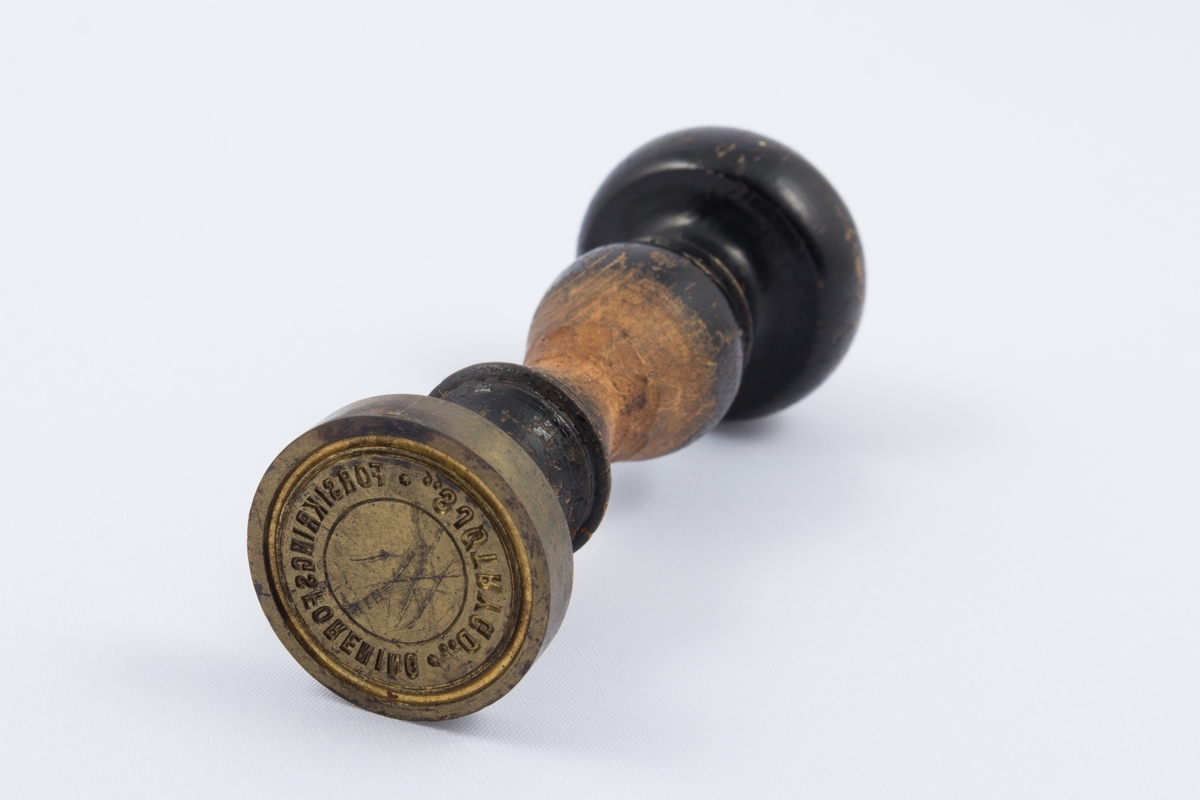 Stempel til Forsikringsforeningen Sjøtrygd med dreid treskaft og stempelhode i messing