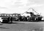 Färjeläget i Gränna hamn. Folk lämnar färjan Hebe V och andra väntar på att gå ombord. En buss med glastak från 