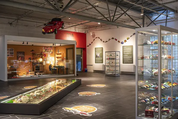 Oversiktsbilde over utstillingen Små biler - store gleder, med glassmontre, sandkasse og "gutterom" med lekebiler.