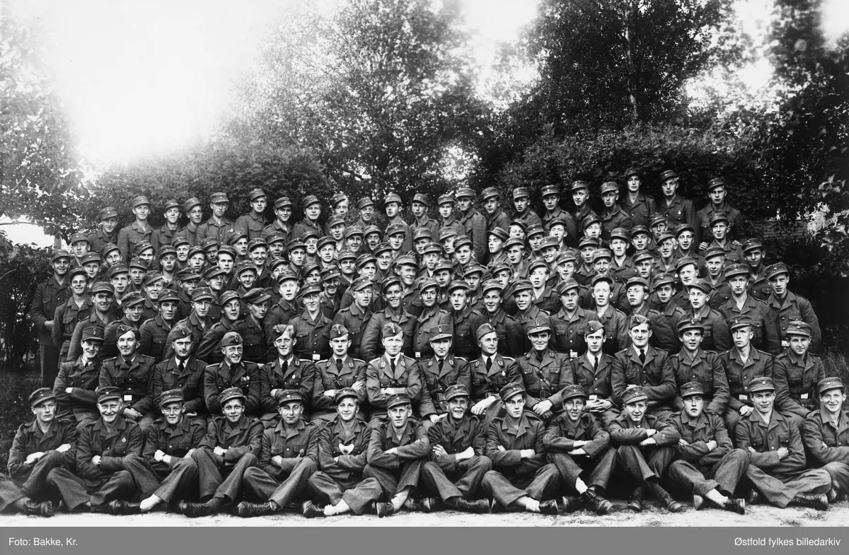 Arbeidstjenesten (AT), gruppe-bilde av mannskap og offiserer, på Folkehøgskolen, Mysen under andre verdenskrig i 1943. Ca. 136 mann. I  midten med båtlue: sveitfører Rust. Til venstre for han nestsveitfører Ekhaugen. Til høyre kvartermester Rud, deretter troppfører Heyerdahl.
Bilde nr. 2 er et utsnitt.