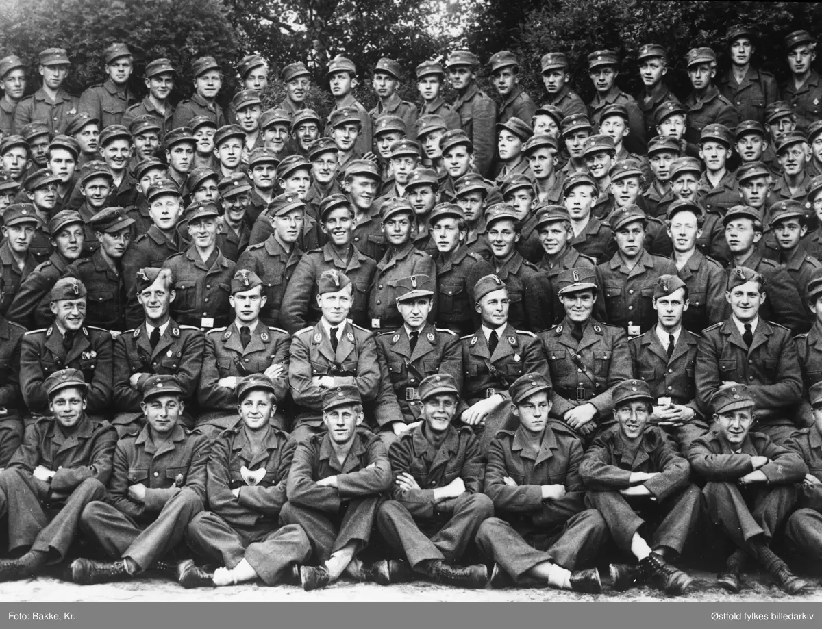 Arbeidstjenesten (AT), gruppe-bilde av mannskap og offiserer, på Folkehøgskolen, Mysen under andre verdenskrig i 1943. Ca. 136 mann. I  midten med båtlue: sveitfører Rust. Til venstre for han nestsveitfører Ekhaugen. Til høyre kvartermester Rud, deretter troppfører Heyerdahl.
Bilde nr. 2 er et utsnitt.