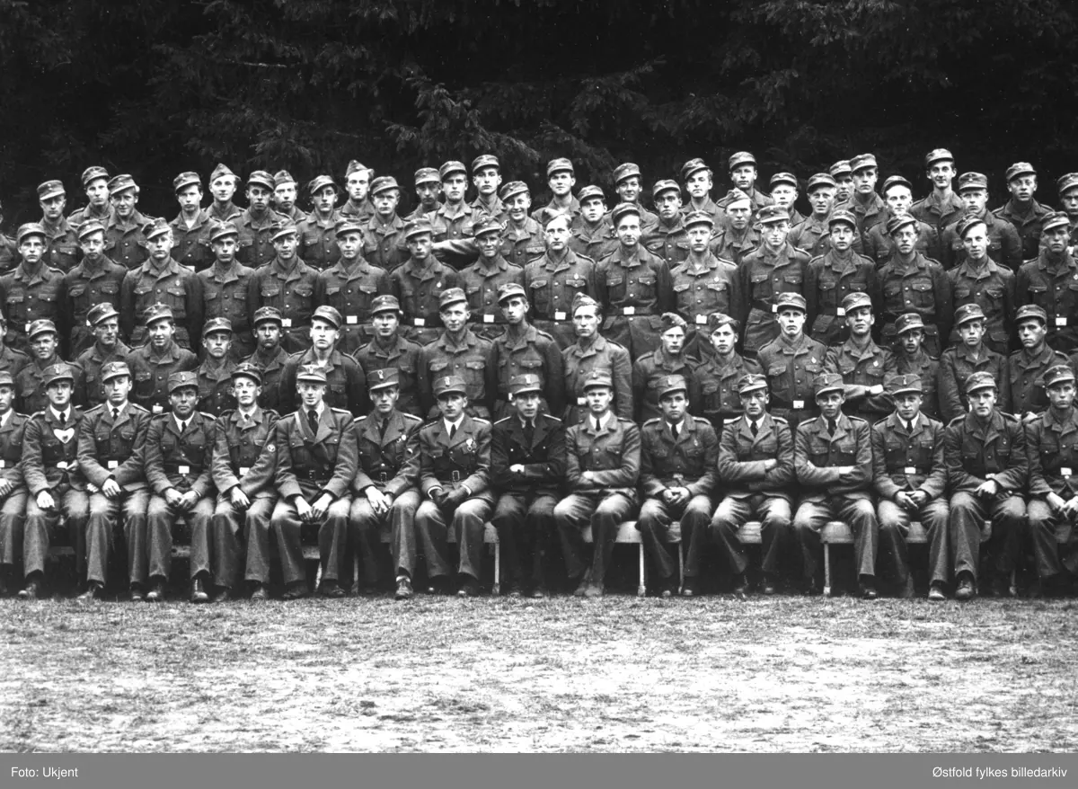 Arbeidstjenesten (AT) under andre verdenskrig, gruppebilde med mannskap og offiserer, utenfor Høysand badehotell i Skjeberg 1942. 
En person er kjent, plassering se fotokort med pålimt utsnitt med kryss under person i første rekke: Sveitfører Grønnerød.