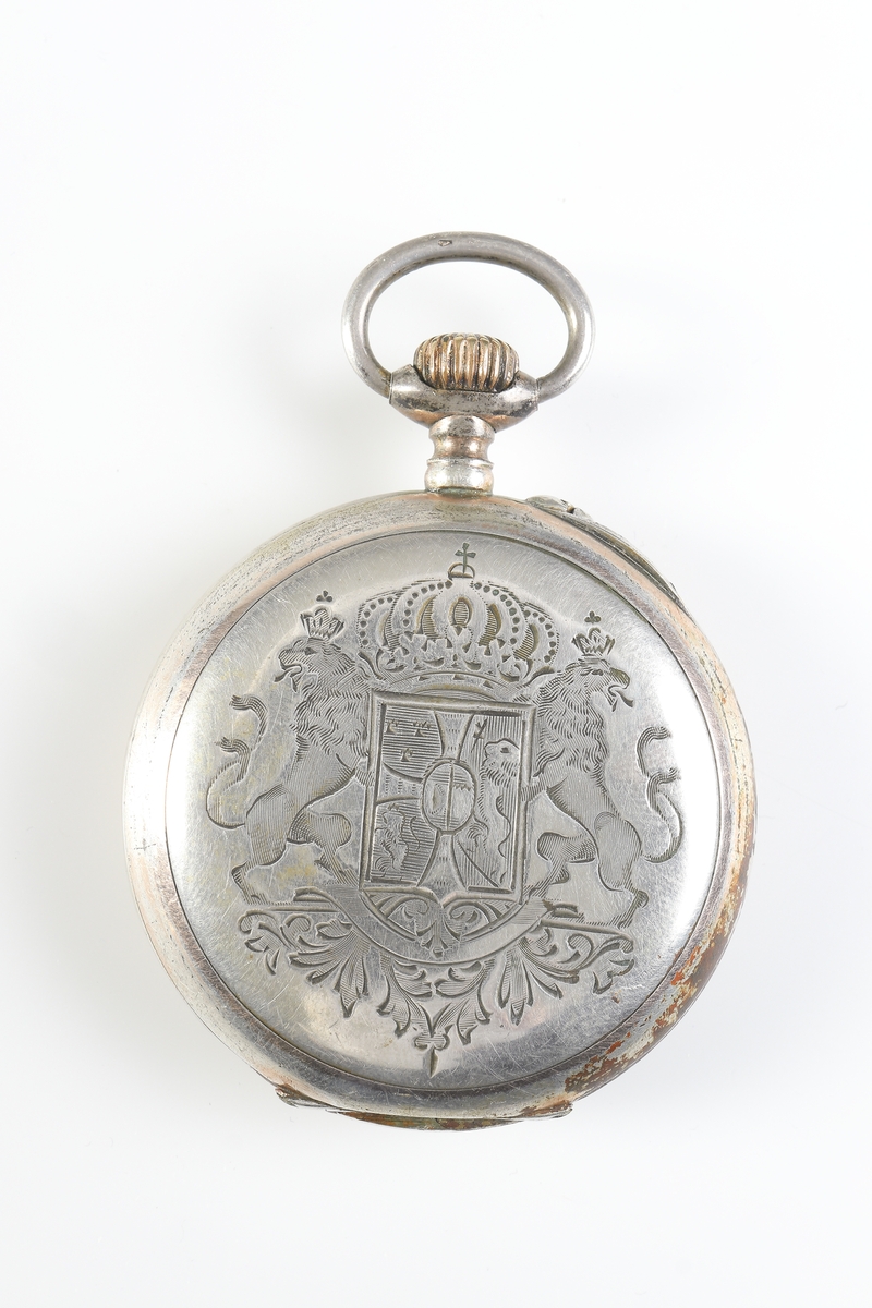 Fickur i silver som dras upp med krona. Runt kronan finns en bygel för att fästa en klockkedja. Den främre boetten har ett glas monterat framför urtavlan som består av vit emalj. Visarna är utsirade i guldfärg, och nedtill en mindre urtavla för sekundvisning. Bakboetten har ett mönstrat motiv liknande det svenska riksvapnet med två lejon på vardera sidan om en sköld krönt med en krona. Boettens ytterkanter är guldförgyllda. Ytterboettens insida har en stämpel liknande en halvmåne och en kungakrona, samt en större och en mindre som liknar en orre. Vidare finns numret "304070" och "0.800" inramat. Även "GALONNE" finns stämplat och siffran "11". Innerboettens utsida har ett graverat mönster bestående av ett liggande lejon med en sköld med de tre svenska kronorna vid sidan om. Vidare finns texten "1/2 CHRONOMETRE REMONTOIR SPIRAL BREGUET" och "CHATON OR 19 RUBIS" samt "BALANCIER COMPENSSÉ". Innerboettens insida har numret "304070" och stämpeln liknande halvmåne och krona inslaget, samt "0.800" inramat. Verket utan stämplar. 
Klockans skyddsboett i två delar, består av en överdel med ett fönster i celluloid, och en underdel att lägga uret i. Baksidan märkt med "23 1/2" och "Herkules D.R.G.M. 160717". Dosan troligen i nickel.